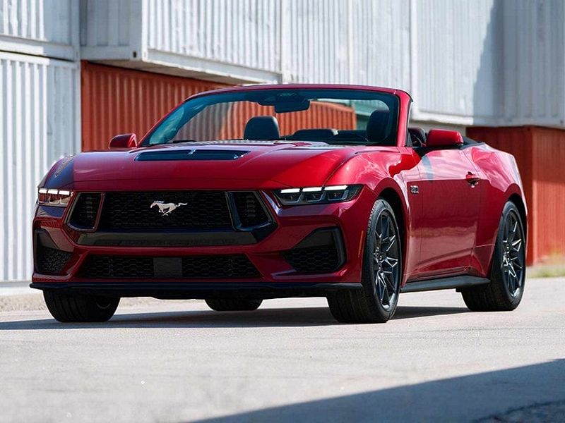 A red Ford Mustang GT convertible with the top down, parked in front of a wall of shipping containers